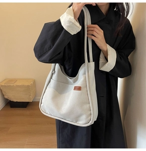 Detailed view of white canvas bucket bag with brown leather logo patch on a black coat