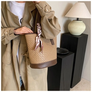 Detail of woven tote bag with leather trim and decorative silk scarf on the handle