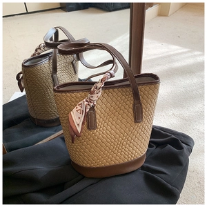 Close-up of woven bucket bag featuring brown leather trim and decorative silk scarf