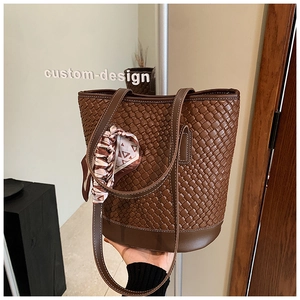 Detail of brown woven bucket bag with elegant geometric scarf on the handle