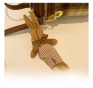Détail d'un charm lapin en tricot attaché à un sac à bandoulière à carreaux marron