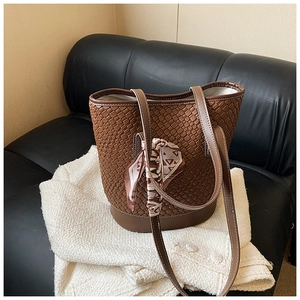 Detailed view of brown woven leather bucket bag with decorative silk scarf and thin strap