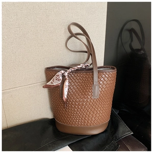Detail of a brown woven bucket bag featuring an elegant geometric silk scarf on the handle