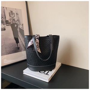 Detail of black woven bucket bag with purple silk scarf on art book in modern setting