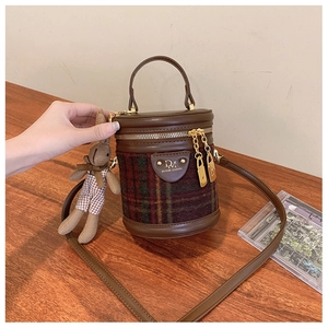 Détail d'un sac seau en tissu écossais vert et rouge avec bordure en cuir et lapin
