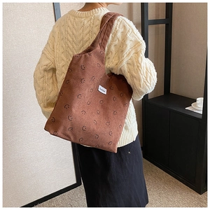 Sac fourre-tout en velours côtelé marron avec motif souriant porté par un mannequin