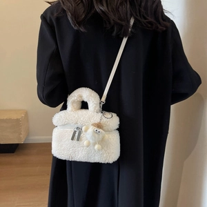 Sac seau minimaliste en peluche blanche avec breloque et bandoulière sur un manteau noir