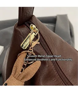 Close-up of brown leather dumpling bag featuring gold metal zipper and cute rabbit charm