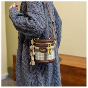 Détail d'un sac seau à carreaux avec breloque lapin en peluche sur pull gris