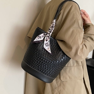 Black woven bucket bag with patterned silk scarf handle on a model in trench coat