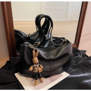 Detail of black pleated faux leather hobo bag with a cute plush bunny charm and gold buckle