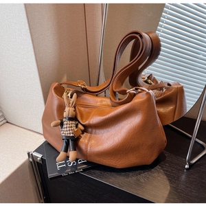 Detail of a brown leather hobo bag with a rabbit charm on a dark wooden surface