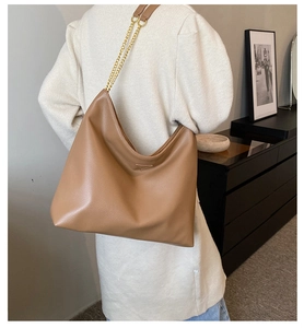 Détail du sac seau marron avec texture litchi et bandoulière en chaîne dorée dans le salon