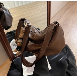 Detail of dark brown faux leather hobo bag with gold buckle and rabbit doll pendant