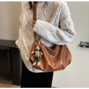 Brown leather hobo bag with adjustable strap and cute rabbit charm in a cozy winter setting