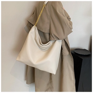 Détail du sac cabas en cuir crème avec chaîne dorée sur un trench-coat beige classique