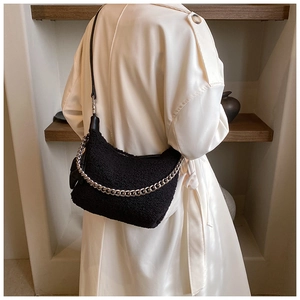 Détail du sac croissant en laine bouclée noire avec chaîne argentée porté sur un trench