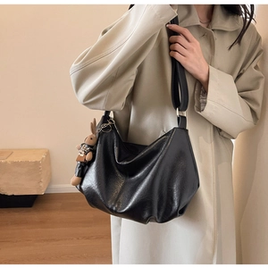Detail of a black pleated hobo bag with a rabbit charm on a wide shoulder strap