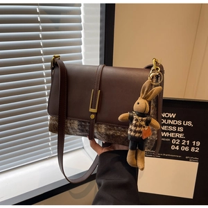 Detail of a brown crossbody bag with metal buckle and a cute brown rabbit pendant