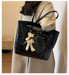 Close-up of a black padded tote bag with a beige knit bear charm on a shoulder strap