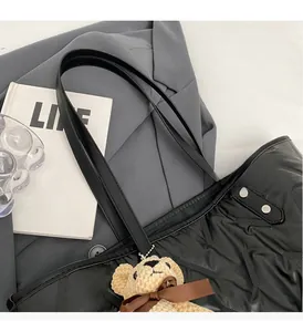 Detail of black quilted tote bag with reinforced handles and plush bear charm decoration