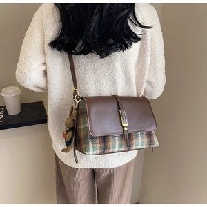 Detail of retro flap shoulder bag in brown leather and plaid tweed with a plush rabbit charm