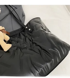 Detail of black quilted tote bag with soft texture and a cute beige bear charm pendant