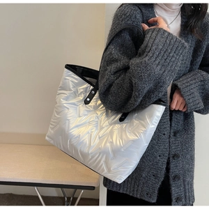 Silver quilted tote bag with black leather handles shown from a side view on a model