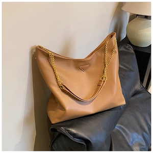 Détail du sac hobo en cuir grainé caramel avec bandoulière en chaîne dorée sur sofa