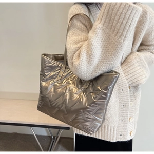 Detail of metallic quilted tote bag with chevron stitching held by a woman in beige knit
