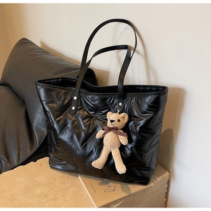 Detail of black quilted tote bag with bear charm on a stone base and neutral background