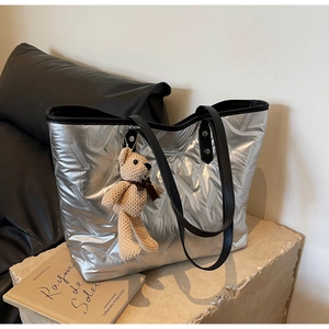 Detail of silver quilted tote bag with black leather handles and cute bear pendant