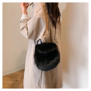 Detalle de un bolso bandolera redondo de pelo sintético negro con cadena sobre gabardina