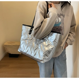 Detail of silver quilted tote bag with metallic finish and black reinforced handles