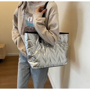 Detail of silver metallic quilted tote bag with down fabric texture and black straps