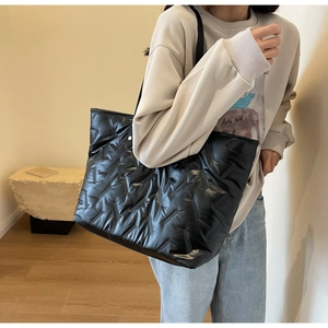 Side view of large black quilted tote bag in shiny nylon fabric worn by a model