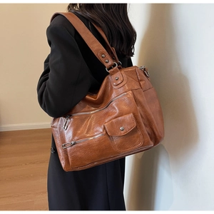 Detail view of large brown leather tote showing vintage texture and multiple zippered pockets