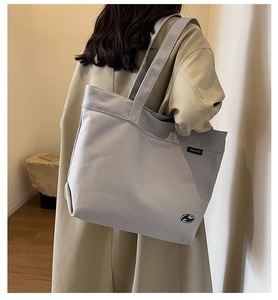Vista lateral de un gran bolso tote de lona con etiqueta llevado por modelo con abrigo