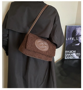 Detail of dark brown plush shoulder bag with oval logo on a black coat outfit