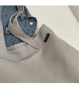 Detalle del bolso tote de lona gris claro con textura de tela y etiqueta de marca tejida