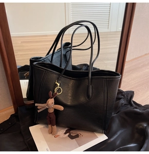 Detail of black large tote bag featuring shiny leather texture and cute bunny pendant