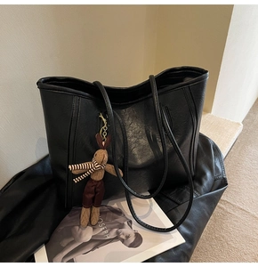 Detail of black textured leather tote bag with a cute rabbit charm and magazine decor