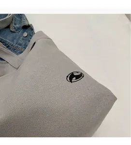 Detalle del bolso tote de lona gris claro que muestra la textura y el diseño del logo