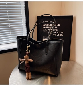 Detail of black tote bag featuring crinkled leather texture and a plush rabbit charm