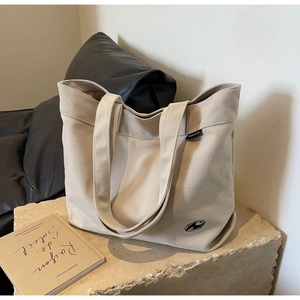 Detalle del bolso tote de lona beige con logotipo negro sobre superficie de piedra