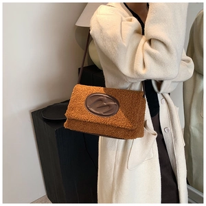Detail of plush brown teddy shoulder bag featuring embossed leather M patch and slim straps
