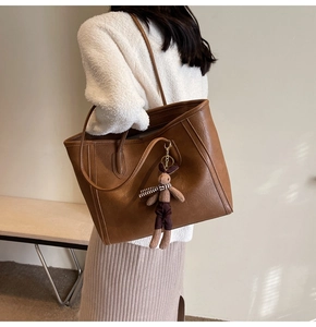 Brown leather tote bag detail with striped scarf rabbit plush charm on a long handle