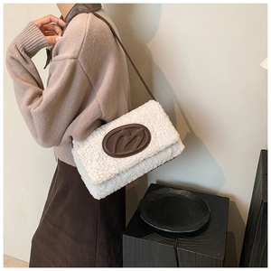 Close-up of white fleece shoulder bag with a brown leather M patch and slim strap