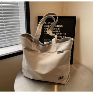 Primer plano del bolso tote de lona beige con etiqueta de logo sobre mesa de metal
