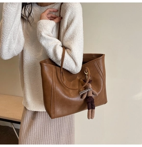 Detail of retro brown tote bag with leather texture and plush bear pendant on model